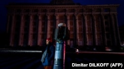 O femeie, în piața întunecată din fața clădirii avariate a Administrației Regionale de Stat din Harkov, pe 5 noiembrie 2022, după ce rachetele ruse au lovit rețelele de electricitate