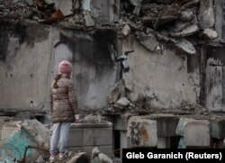 Një vajzë e vogël duke shikuar muralin e Banksyt në cepin e një ndërtese të shkatërruar nga raketat ruse.