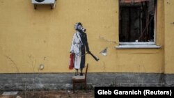 Një grua me robdeshambër, flokët me lidhëse për kaçurrela, e në fytyrë ka të vendosur një maskë kundër gazit, në dorë mban një pajisje për fikjen e zjarrit.