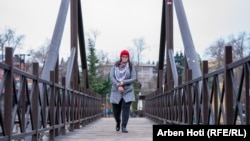Ndalore Likaj rregullon mëngën e palltos derisa kalon mbi një urë pranë një parku në Prizren.