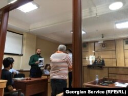 ედუარდ მარიკაშვილი მოწმე პოლიციელს აჩვენებს ფოტოს, რომელიც 2 ივნისის ღამეს არის გადაღებული პარლამენტის შენობასთან. ამ ფოტოზე მარიკაშვილს სუფთა, უწარწერო ფურცელი უჭირავს ხელში.