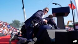 В секундите след стрелбата агенти на Сикрет сървис ограждат Доналд Тръмп, който вече се е скрил зад подиума. 