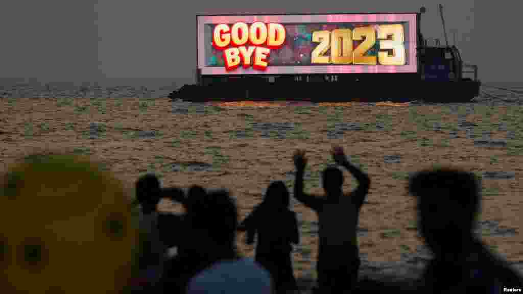 Az emberek az év utolsó naplementéjét nézik egy strandról szilveszterkor az indiai Mumbaiban 2023. december 31-én