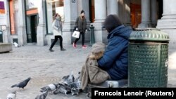 Egy koldus takaróba bugyolálva fog egy gyereket, miközben galambokat etet egy hideg téli napon Brüsszel központjában, Belgiumban 2018. február 28-án