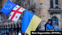 Një protestuese në Tbilisi duke mbajtur flamujt e Bashkimit Evropian, Gjeorgjisë dhe Ukrainës, në një marsh për të shënuar përvjetorin e dytë të luftës së nisur prej Rusisë në Ukrainë.