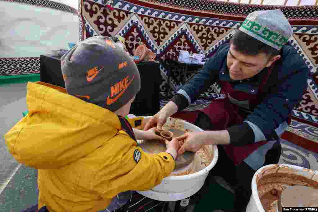 Мастер обучает мальчика гончарному искусству на праздничной ярмарке&nbsp;