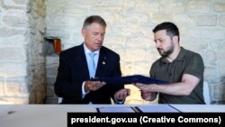 Președintele român, Klaus Iohannis, și cel ucrainean, Volodimir Zelenski, semnând acorduri de colaborare între țările lor, în timpul summitului Comunității Politice Europene de la Bulboaca, în iunie 2023 