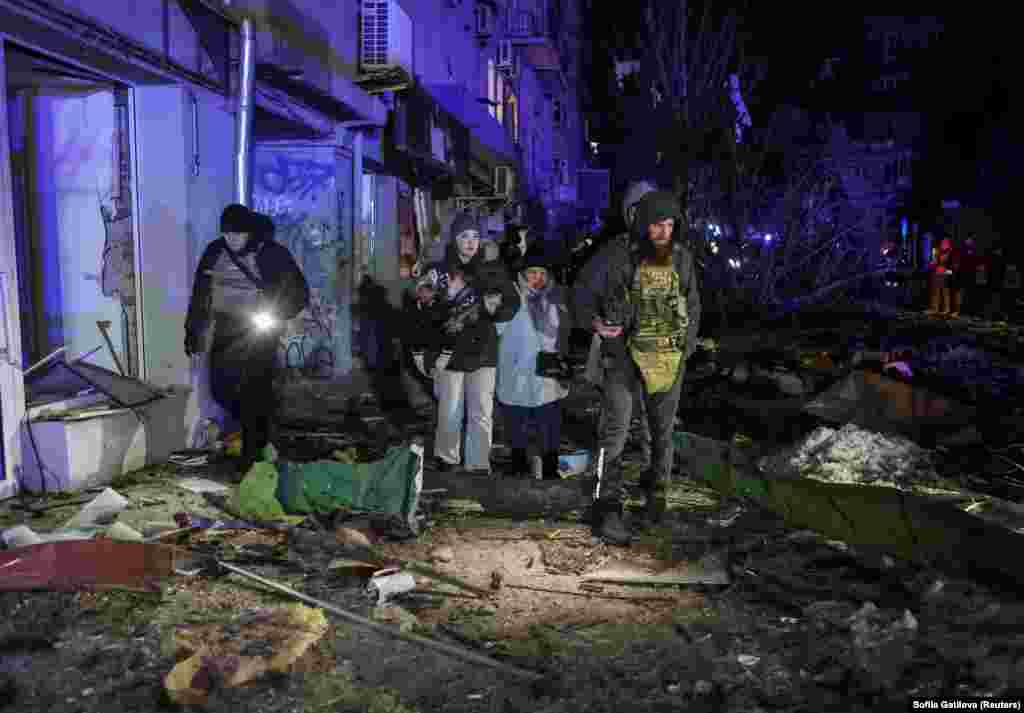 Radnici hitne pomoći pomažu stanovnicima da prođu kroz ruševine nakon što su bili prisiljeni napustiti svoje oštećene domove nakon napada.