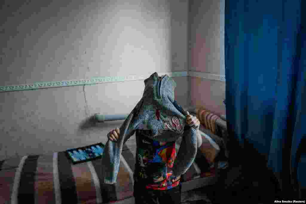 Ruslan, în vârstă de 9 ani, un refugiat din Toretsk, își pune un rând de haine în plus.&nbsp; Familiile cu copii stau, de obicei, câteva zile în adăpost, în timp ce persoanele evacuate mai în vârstă, cărora le este mai greu să găsească locuințe permanente, stau uneori luni de zile.