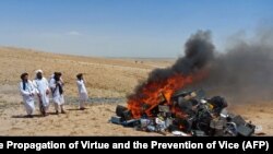 Припадниците на талибанската полиција за морал стојат покрај огнот со музички инструменти и опрема што тие ги конфискуваа и запалија во западниот авганистански град Херат на 29 јули.