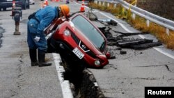 Работник стои до кола, заседнала в разбит път след земетресение в префектура Ишикава, Япония, 3 януари 2024 г. Към 5 януари беше съобщено, че жертвите след труса от 7,6 по Рихтер в Япония на 1 януари, са повече от 90 и броят им не спира да расте. Стотици са и разрушените сгради. 
