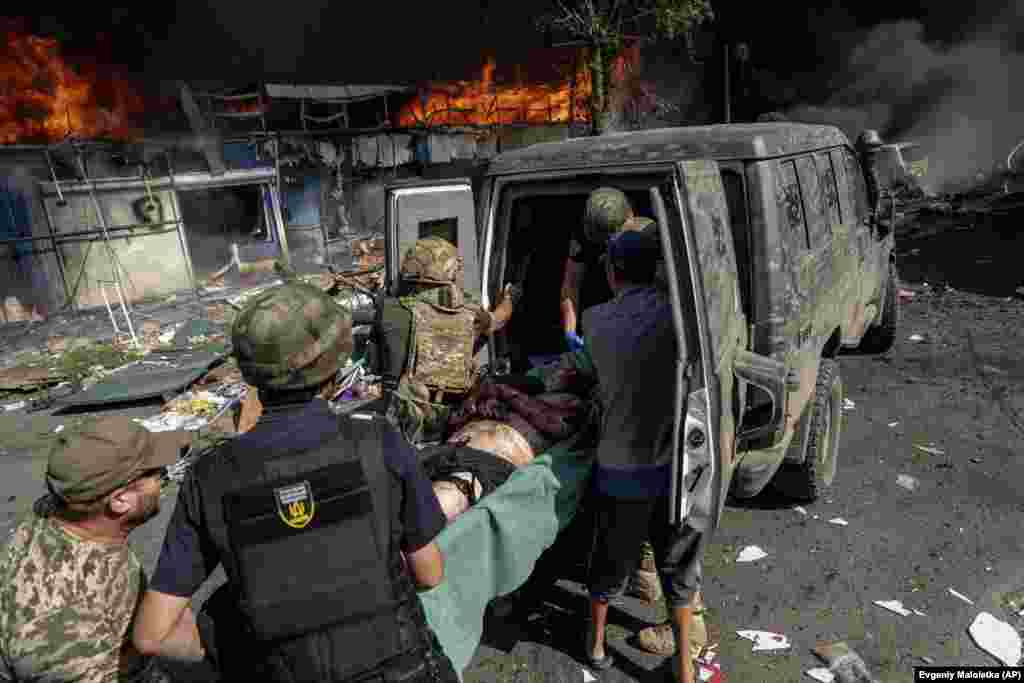 Un rănit este transportat la ambulanță. În fundal, piața incendiată..