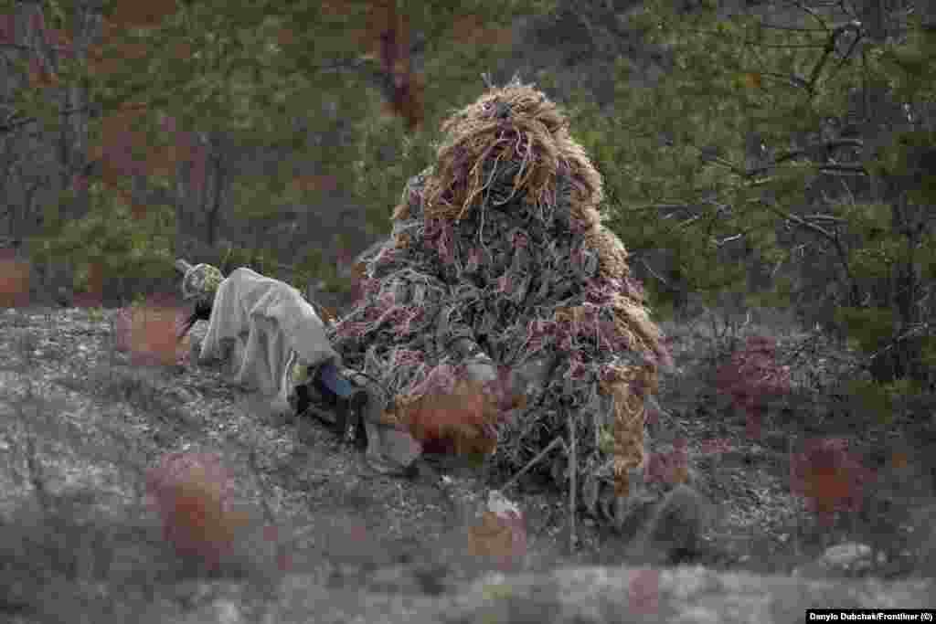 Katerina, snajperistica pod pseudonimom, razgovora s novinarima ispod svoje kikimore. Ona se obučava za kamuflažu, što je umjetnost za sebe. &quot;Ako ste odabrali položaj u kojem ćete ležati, ne možete uvijek pratiti svoje noge, svoje oružje&quot;, objašnjava Katerina. &quot;Na primjer, nož s pojasom može zasvijetlili na otvorenom. Sve to morate uzeti u obzir&quot;, kaže ona. Na obuci &quot;instruktori šetaju okolo, gledaju naše položaje, ukazuju na greške, slikaju, onda sve analiziramo&quot;, kaže Katerina.