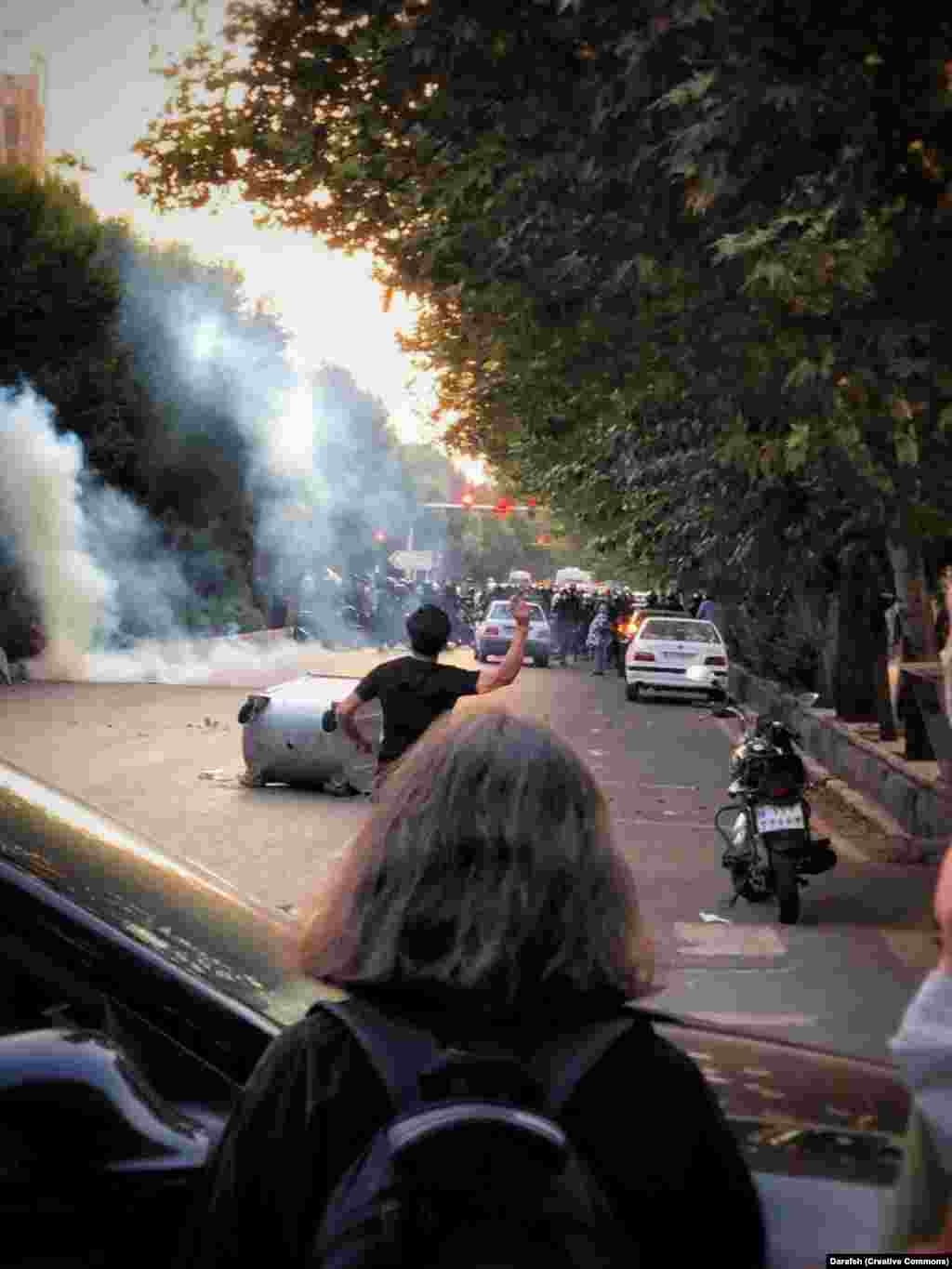 O fotografie din 2022 septembrie arată o tânără care privește protestele violente din Teheran, după moartea Mahsei Amini. De-a lungul tulburărilor din toată țara care au urmat morții Mahsei Amini în septembrie 2022, în timp ce se afla în custodia poliției pentru moralitate, tot mai multe femei au decis să nu poarte hijabul. Eșarfele de pe cap au devenit obligatorii în Iran la scurt timp după Revoluția islamică din 1979.