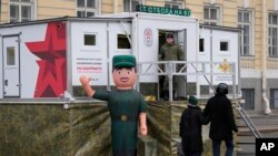 Луѓето поминуваат покрај мобилниот центар за регрутирање поставен во близина на воено-историската изложба на плоштадот Дворцоваја во Санкт Петербург, Русија, јануари 2024 година.