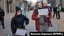 Мариана (с черното яке). На плаката, който държи, пише "Уважаеми управляващи, принуждавате родители да даряват бебешки обувки. Никога неносени".