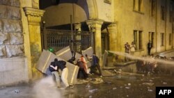 Miting împotriva unui controversat proiect de lege privind „influența străină", la Tbilisi, la 1 mai 2024. Sunt pulverizate tunuri cu apă în timp ce manifestanții încearcă să blocheze intrarea laterală a Parlamentului georgian.