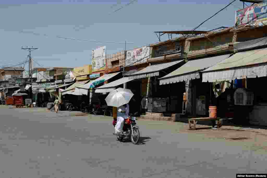 Par koji je stavio kišobran na motocikl &nbsp;vozi se napuštenom pijacom u Džakobabadu. Porast temperature doveo je zatvaranja škola u Pendžabu, što je uticalo na najmanje 26 miliona dece.