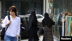 Teheráni nő fejkendő nélkül az utcán 2023. július 16-án. Mögötte két, hidzsábot viselő nő