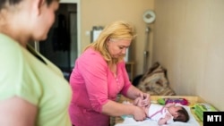 Az MTI fotóján Chrenkó Zoltán Mihályné védőnő nyíregyházi családlátogatásán tisztába tesz egy kislányt 2015. június 9-én