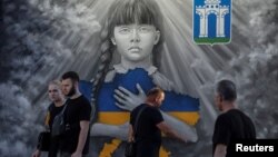 Хора минават покрай патриотичен стенопис на фона на атаката на Русия срещу Украйна. В центъра на Ровно, Украйна, 31 май 2023 г.