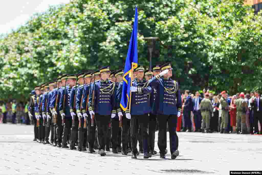 Një pjesëtar i një njësiti të Policisë së Kosovës mban në dorë flamurin e Kosovës teksa parakalon bashkë me oficerë të tjerë në sheshin e Prishtinës më 12 qershor 2024, për nder të Ditës së Çlirimit të vendit.