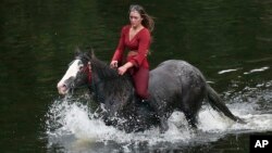 Жена преминава на кон реката по време на Панаира на конете в Апълби. 6 юни 2024 г. Панаирът на конете е ежегодно събиране на туристи и пътешественици в град Апълби, Англия. 