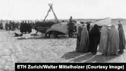 Жени в бурки наблюдават как Мителхолцер ремонтира самолета си на 40 км. от Техеран