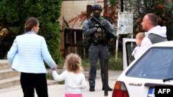 Gyalogosok sétálnak, miközben a koszovói rendőrök átkutatnak egy éttermet és egy másik épületet Mitrovicában 2023. szeptember 29-én, a kolostori lövöldözések után