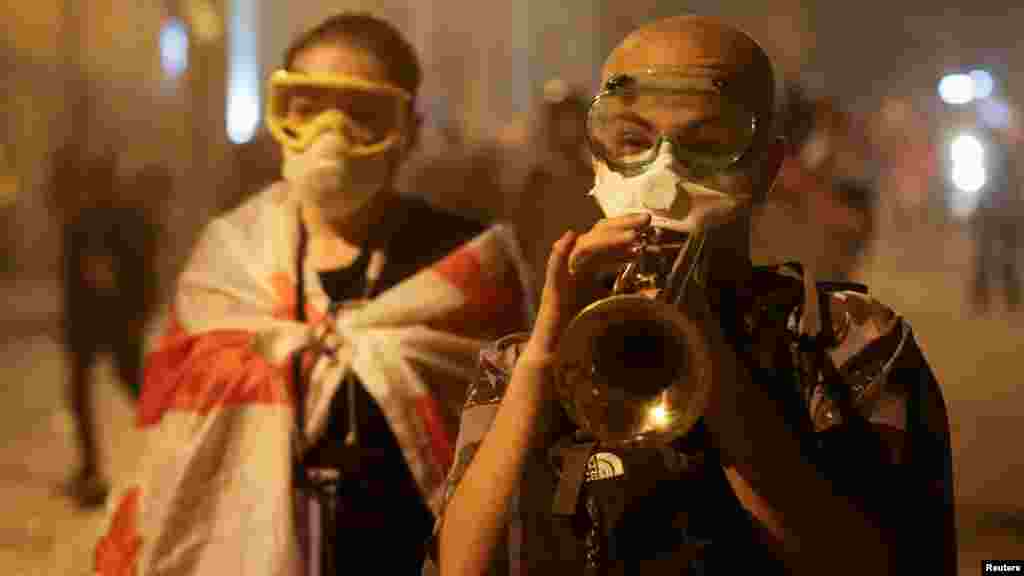 Tüntető trombitával és könnygáz ellen védő maszkban a&nbsp;&bdquo;külföldiügynöktörvény-javaslatról&rdquo; szóló parlamenti vita alatt a georgiai Tbilisziben 2024. május 2-án. A törvény előírná a külföldi finanszírozású civil szervezeteknek, hogy regisztrálják a tevékenységüket, és széles körű felügyeleti jogkörrel ruházná fel a hatóságokat a civilek működésének ellenőrzésére