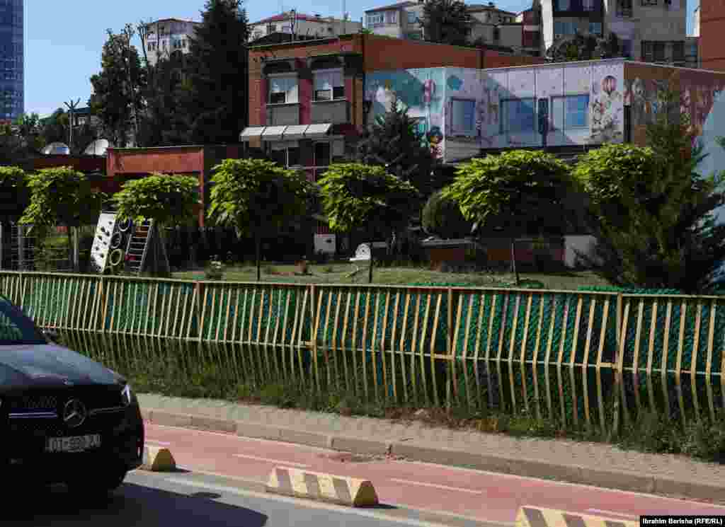 Prishtinë 13 qershor 1999: Ushtarët britanikë derisa shikojnë një objekt banimi kolektiv duke u djegur në Prishtinë. Sipas përshkrimit të fotografisë nga Reuters, kjo fotografi është shkrepur pak kohë pasi trupat britanike ishin sulmuar me armë zjarri nga një pjesëtar i ushtrisë serbe. &nbsp; 5 qershor 2024: Përgjatë viteve shihet se në këtë lokacion është ndërtuar një objekt shkollor, si dhe janë vendosur rrethoja pas zgjerimit të rrugës. Shumë objekte të tjera për banim kolektiv janë ndërtuar në 15 vjetët e fundit. 