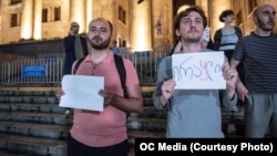 "საქართველოს დემოკრატიული ინიციატივის" თავმჯდომარე ედუარდ მარიკაშვილი თეთრი ფურცლით და აქტივისტი ნიკა რომანაძე ქაღალდზე დაწერილი წარწერით "ირა*ლი" დაკავებამდე რამდენიმე წუთით ადრე; 2 ივლისი, 2023 წელი