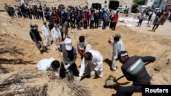 Работници преместват телата на убити палестинци от гроб, разкрит в болницата „Насър“, 21 април 2024 г.