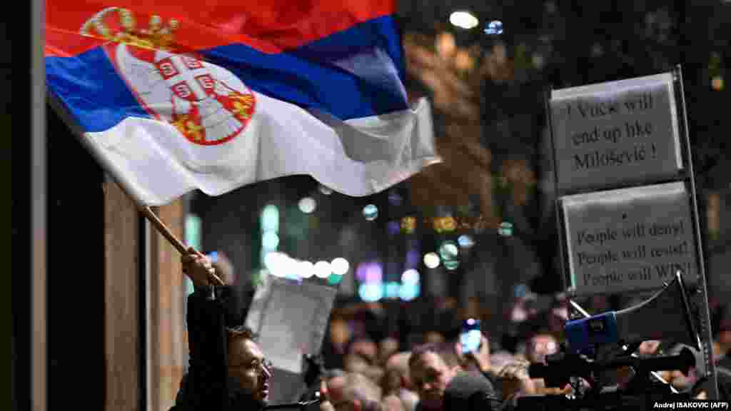 Egy tüntető szerb zászlót tart a választási bizottság épülete előtt Belgrádban 2023. december 18-án, egy nappal a parlamenti és helyhatósági választások eredményhirdetése után.&nbsp;Aleksandar Vučić szerb elnök pártja nyerte Szerbiában az előrehozott választásokat vasárnap