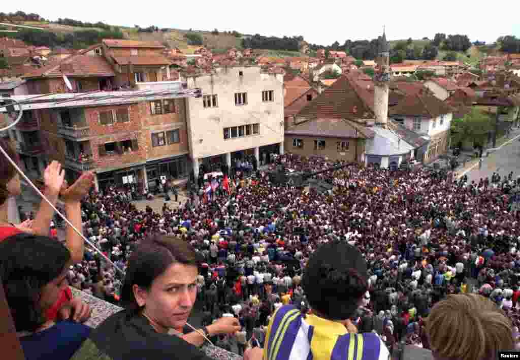 Rahovec 10 korrik 1999: Mijëra qytetarë kishin dalë këtë ditë në qendër të qytetit në Rahovec në ditën e katërt të protestës kundër një dislokimi të mundshëm të trupave paqeruajtëse ruse. Qytetarët shqiptarë të Rahovecit kishin protestuar për disa ditë duke thënë se paraushtarakët rusë kishin marrë pjesë në dhunën serbe kundër tyre. &nbsp; 6 qershor 2024: Përveçse është zvogëluar hapësira e sheshit, xhamia është rrënuar dhe ndërtuar një e re. Disa objekte që shihen para 25 vjetësh ende janë aty, vetëm se kanë pamje tjetër të jashtme. 