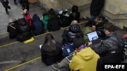 Ljudi provjeravaju informacije na svojim uređajima na stanici podzemne željeznice u Kijevu tokom vazdušnog napada u martu 2023. 