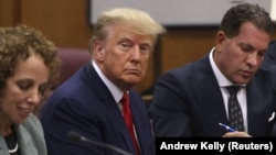  În timpul procedurii de trimitere în judecată, Donald Trump pare îngândurat și privește meditativ mai degrabă prin obiectivul aparatului de fotografiat decât către acesta.