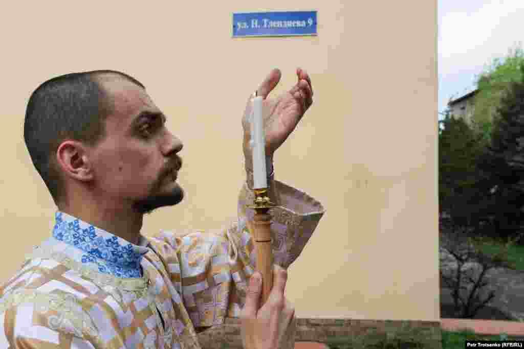 Служитель церкви прикрывает свечу, чтобы не погасло пламя