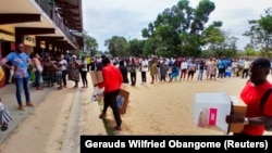 Zvaničnici nose glasačke kutije dok ljudi čekaju otvaranje biračkog mesta tokom predsedničkih izbora u Librevilu, Gabon, 26. avgust 2023.