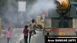 Deca trče za kamionom koji prska vodu po ulici, Nju Delhi, 28. maj 2024.