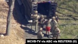 Mladić u crvenom šorcu je Džek Tešer, u trenutku u kom ga agenti FBI sa lisicama na rukama sprovode nakon što je uhapšen u svojoj kući u Masačusecu 13. aprila 2023. dok je prizor hapšenja iz helikoptera beležila kamera.