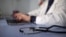 Unknown location -- A stethoscope on the table on the background of a doctor typing on a laptop