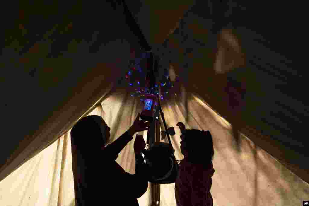 Randa Baker, koja je raseljena zbog izraelskog bombardiranja Pojasa Gaze, vješa ramazanske ukrase i lampione sa kćerkom, obilježavajući početak mjeseca ramazana u improviziranom šatorskom kampu u oblasti Muwasi, na jugu Pojasa Gaze, 11. marta. &quot;Početak ramazana je bio tužan i prekriven mrakom, sa ukusom i smradom krvi posvuda. Izraelska okupacija ne želi da imamo bilo kakvu radost tokom ramazana. Nemamo hrane za naš iftarski sto&quot;, rekao je za AFP&nbsp;raseljeni Palestinac, 50-godišnji Awni al-Kayyal.