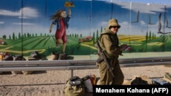 Izraeli katona áll egy falfestmény előtt a Nahal Oz kibuc közelében, a Gázai övezet határán 2023. október 15-én