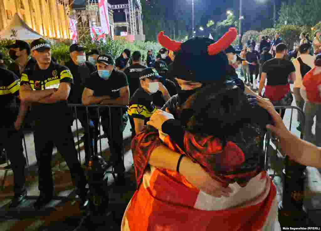 Oameni se îmbrățișează lângă un cordon de securitate, în apropierea clădirii parlamentului din Tbilisi. Partidul de guvernământ &bdquo;Visul Georgian&rdquo; și-a anunțat planurile de a reintroduce proiectul de lege, după ce o versiune anterioară a fost abandonată în 2023. Această nouă versiune omite sintagma &bdquo;agent străin&rdquo;.