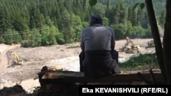 კაცი უყურებს შოვის დამეწყრილ ტერიტორიას, სადაც მძიმე ტექნიკა მუშაობს.