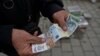 Уличен продавач покажува банкноти со српскиот динар во градот Грачаница, централно Косово, 1 март 2024 г.