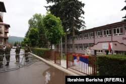 Pjesëtari i KFOR-it hap bllokadën për të mundësuar kalimin e një banoreje nga ndërtesa afër objektit të komunës.