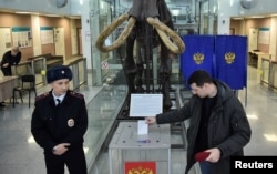 Un ofițer de poliție supraveghează un bărbat ce aruncă buletinul de vot în urnă la secția de vot a Universității de Stat din Novosibirsk, Rusia, pe 17 martie.