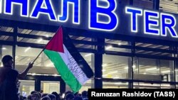 Un bărbat flutură un steag palestinian cu un mesaj pe care scrie „Daghestan este cu voi” în timpul unui miting pro-palestinian la aeroportul din Mahacikala, după aterizarea unui avion din Tel Aviv. Rusia, 29 octombrie 2023.